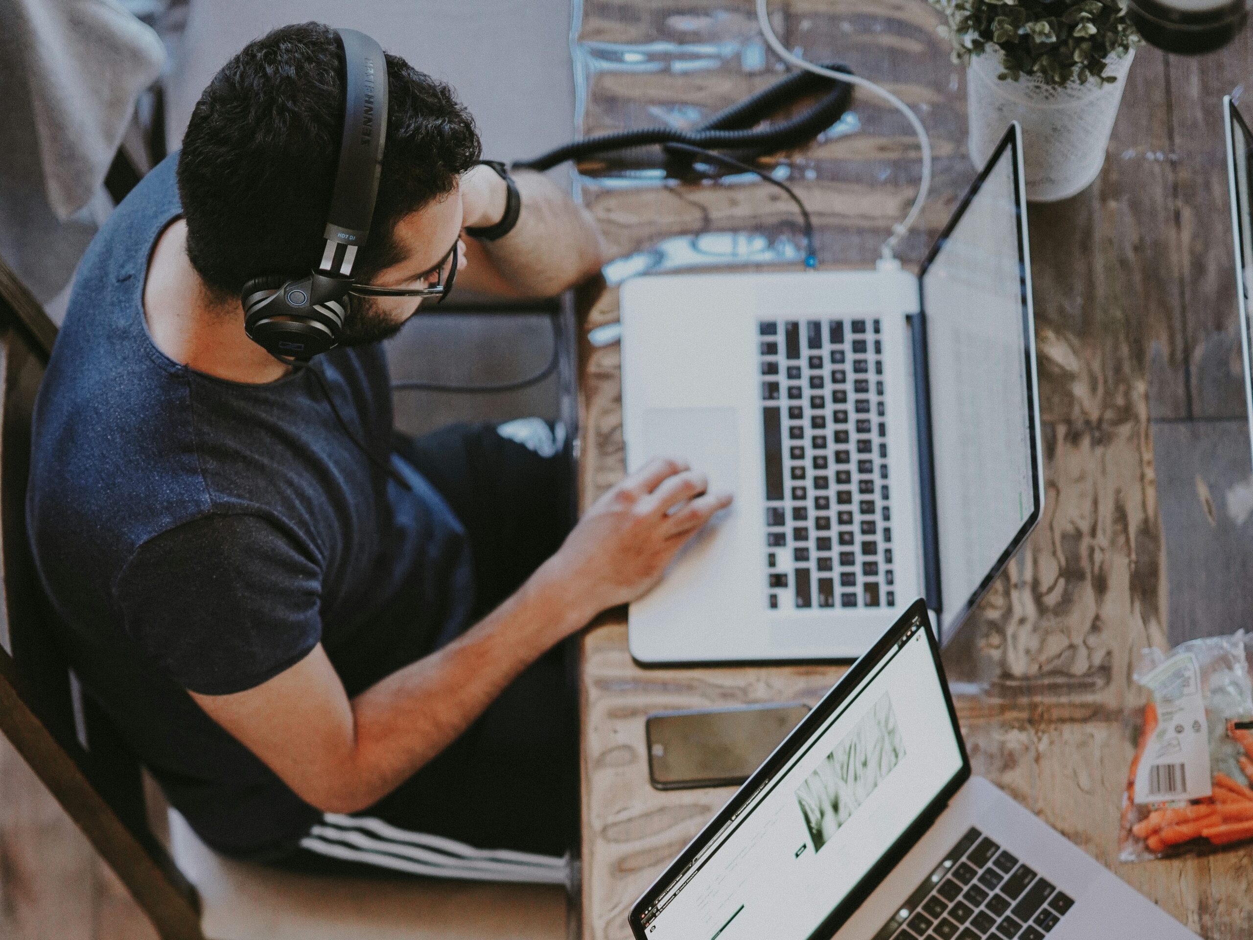 A man with dark hair and wearing casual clothes using a laptop and headphones.